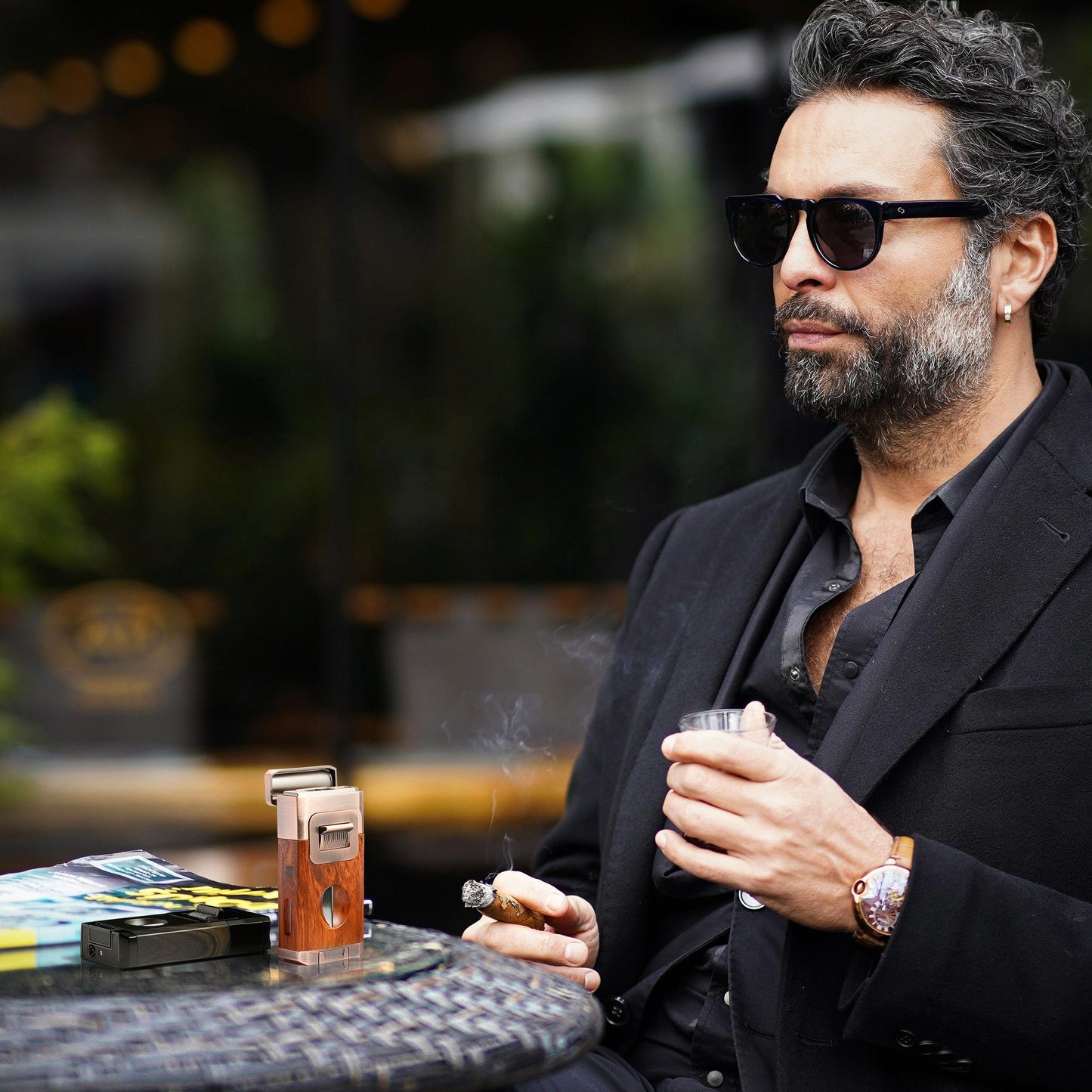 Sophisticated man enjoying a cigar with the rosewood lighter in an outdoor café, showcasing luxury cigar lifestyle.