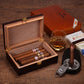 A lifestyle shot of an open cigar humidor filled with cigars, styled with a glass of whiskey, a cigar ashtray, a cigar cutter, matchboxes, and a closed COHIBA humidor in the background, all on a rustic wooden surface.