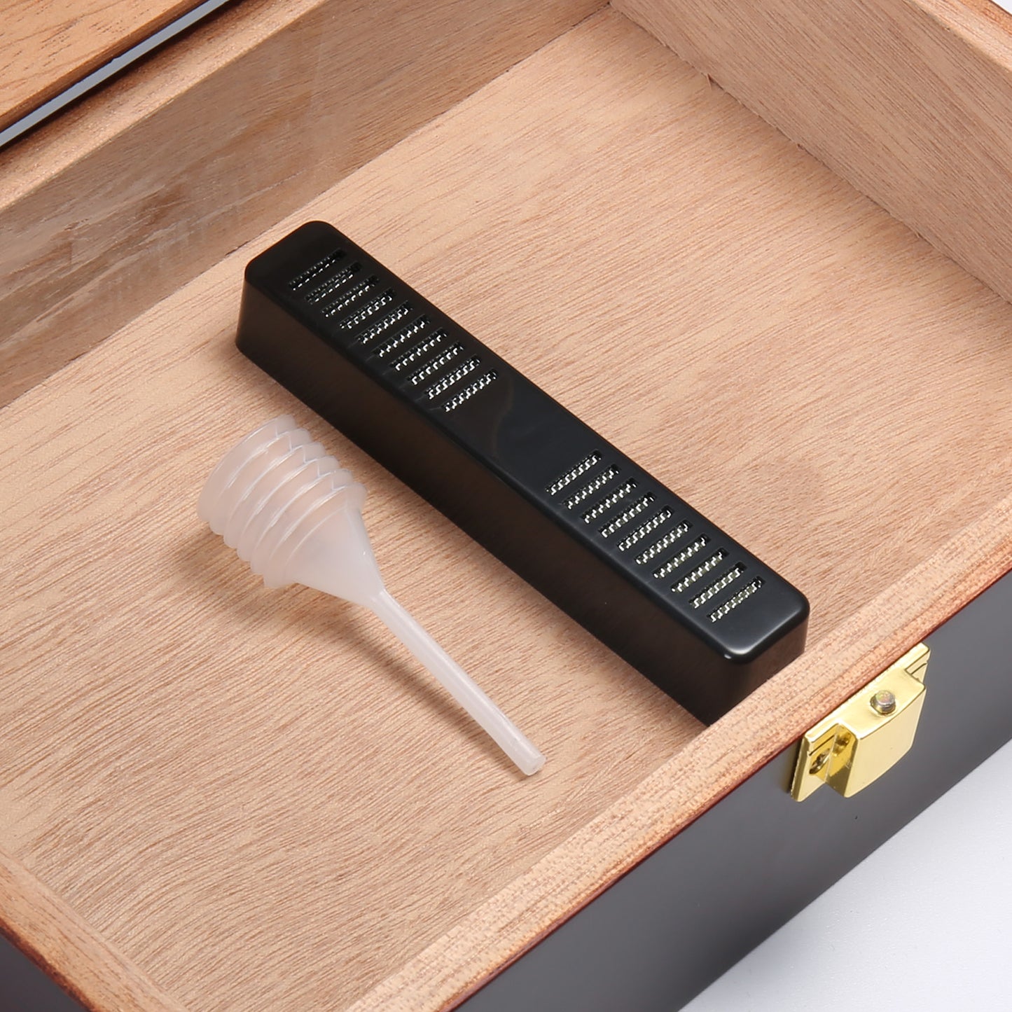 A close-up view of a black removable humidifier and a clear plastic dropper placed on the light brown cedar wood lining inside the humidor.