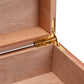 A close-up of the gold-colored metal hinge connecting the lid and base of the humidor, set within the light brown cedar wood interior.