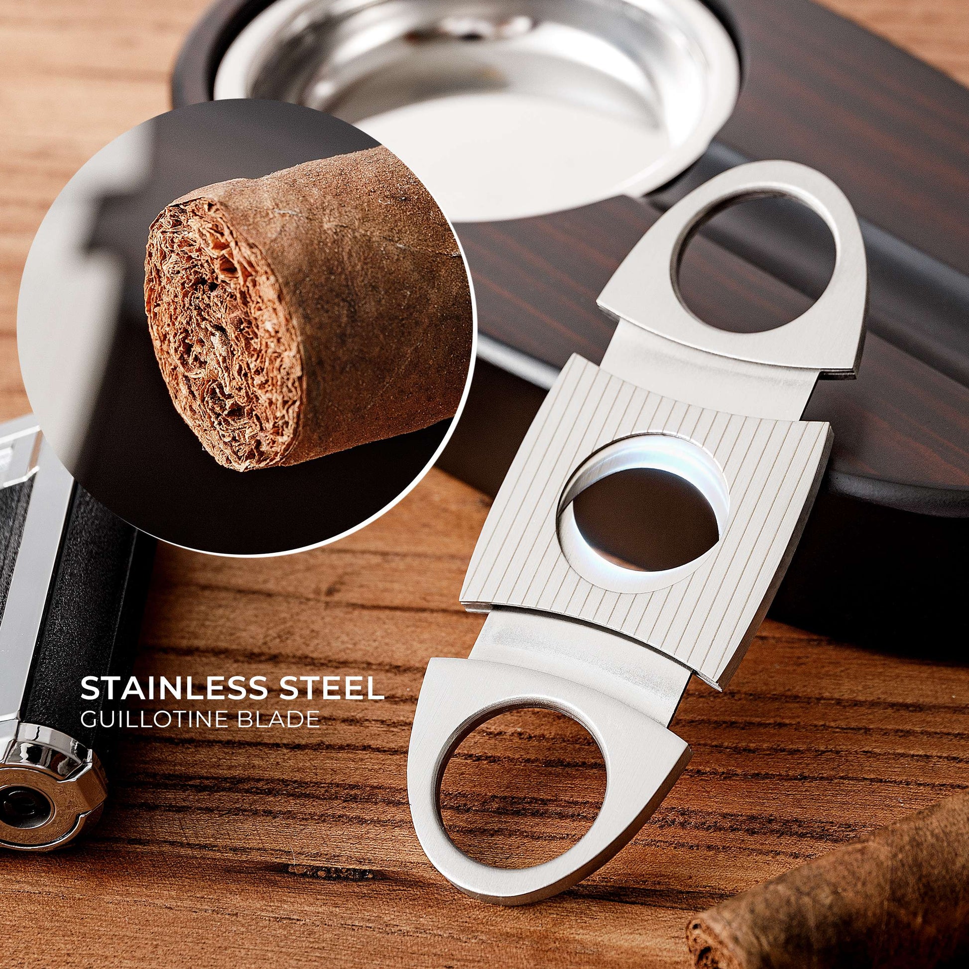 A close-up of a stainless steel guillotine cigar cutter, featuring a textured grip and sharp dual blades, with a magnified inset showing a cut cigar end, labeled "STAINLESS STEEL GUILLOTINE BLADE".