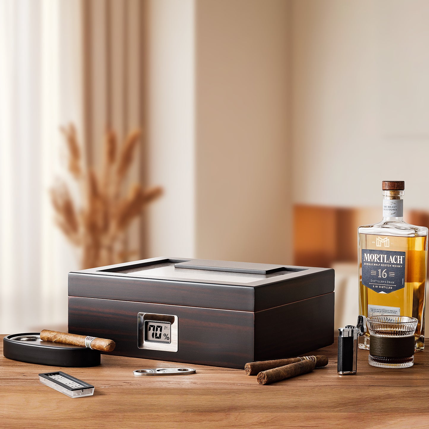 A sophisticated lifestyle scene featuring the large-capacity dark wood cigar humidor, Mortlach whiskey bottle and glass, cigars, cutter, ashtray, and lighter, arranged on a wooden table in a bright, modern interior.