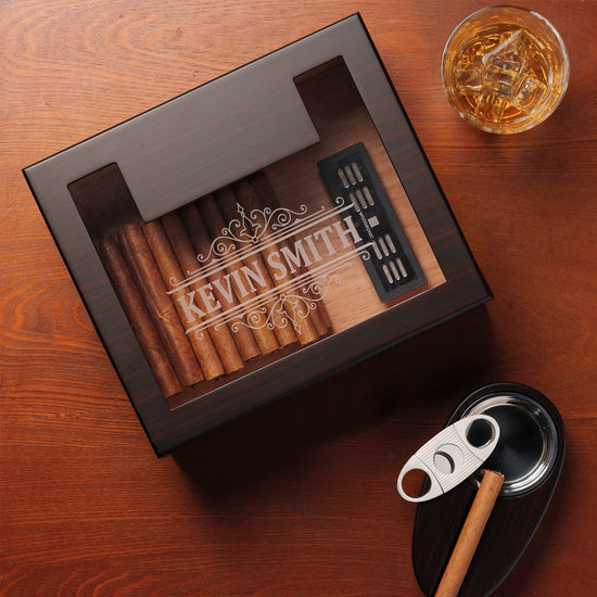 A personalized dark wooden cigar humidor with a glass top, engraved with 