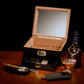 A sophisticated lifestyle scene featuring the open humidor filled with cigars, paired with a Dalmore whiskey bottle, glass, ashtray, cutter, and cigar case, on a wooden table.