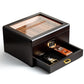 An open humidor revealing its cigar-filled interior, with the pull-out drawer extended to display a stainless steel cigar cutter and wooden cigar lighter, against a white background.