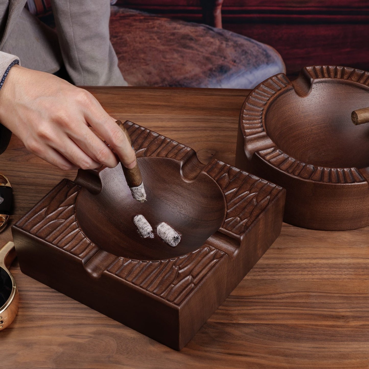 Two wooden cigar ashtrays (square and round) on a home bar table, paired with cigars and whiskey for a luxury vibe.