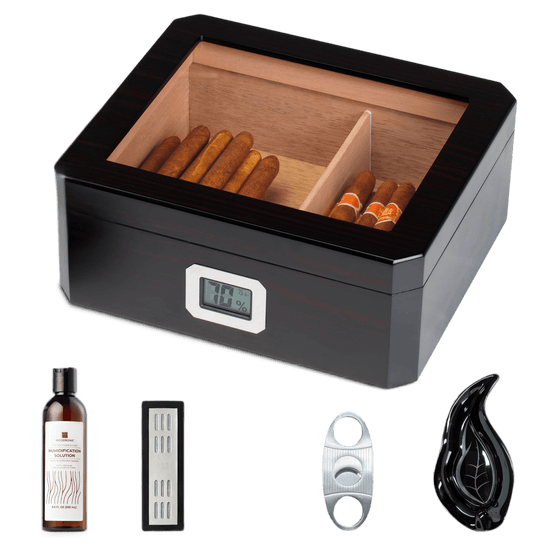 A dark wooden cigar humidor with a glass top and digital hygrometer, displayed with its full accessory set: humidification solution, crystal gel humidifier, stainless steel cigar cutter, and leaf-shaped cigar ashtray, against a white background.