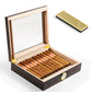 An open cigar humidor displaying its light cedar wood interior, filled with premium cigars, alongside a separate gold humidifier bar, with gold hinges visible on the lid.