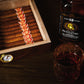 A moody lifestyle shot of the humidor filled with cigars, paired with a bottle and glass of aged whiskey, creating a premium, sophisticated aesthetic for cigar enthusiasts.