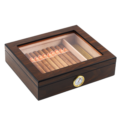 A closed dark wooden cigar humidor with a clear glass top, revealing neatly arranged cigars inside, featuring a gold-rimmed hygrometer on the front panel, set against a white background.