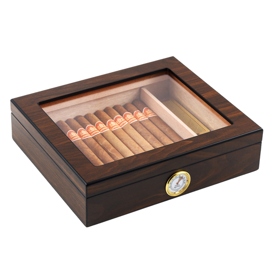 A closed dark wooden cigar humidor with a clear glass top, revealing neatly arranged cigars inside, featuring a gold-rimmed hygrometer on the front panel, set against a white background.