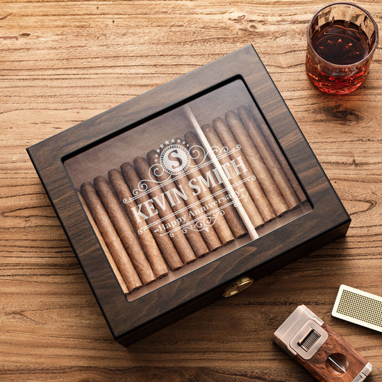 A personalized dark wooden cigar humidor with a glass top, engraved with 