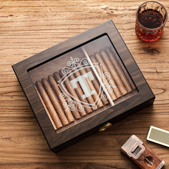 A custom dark wooden cigar humidor with a glass top, showcasing a shield-style monogram 