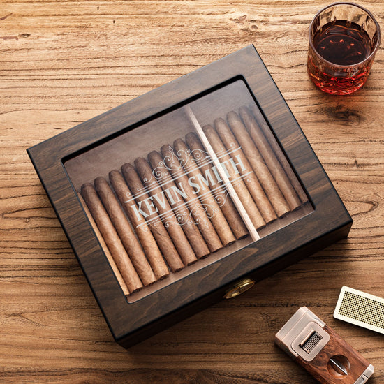 A personalized dark wooden cigar humidor with a glass top, engraved with 