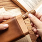 Close-up of hands inserting a premium labeled cigar into the cedar wood slot of a tan leather cigar holder, styled on vintage paper and book pages.