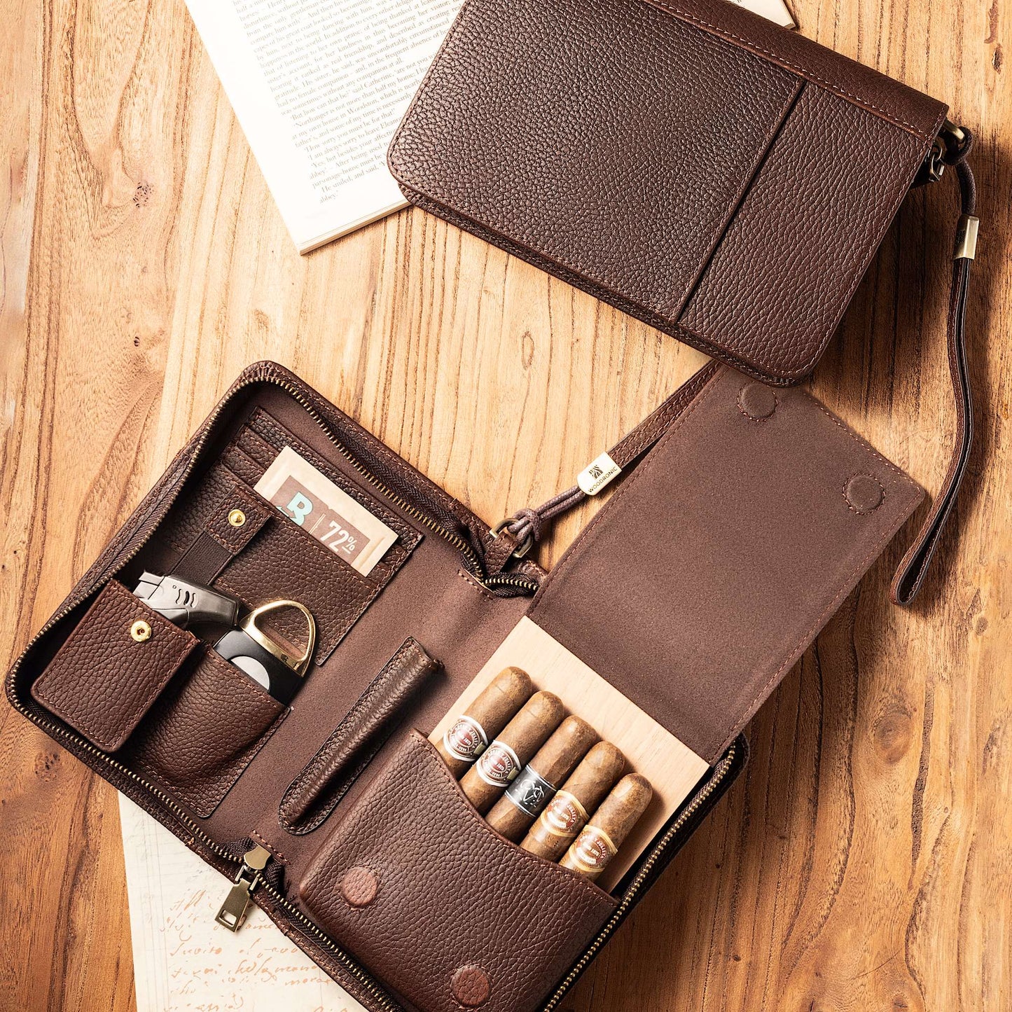 Open leather cigar case laid on a rustic wooden table, displaying its organized interior with five premium cigars, cutter, lighter, and humidifier, styled with vintage book pages.