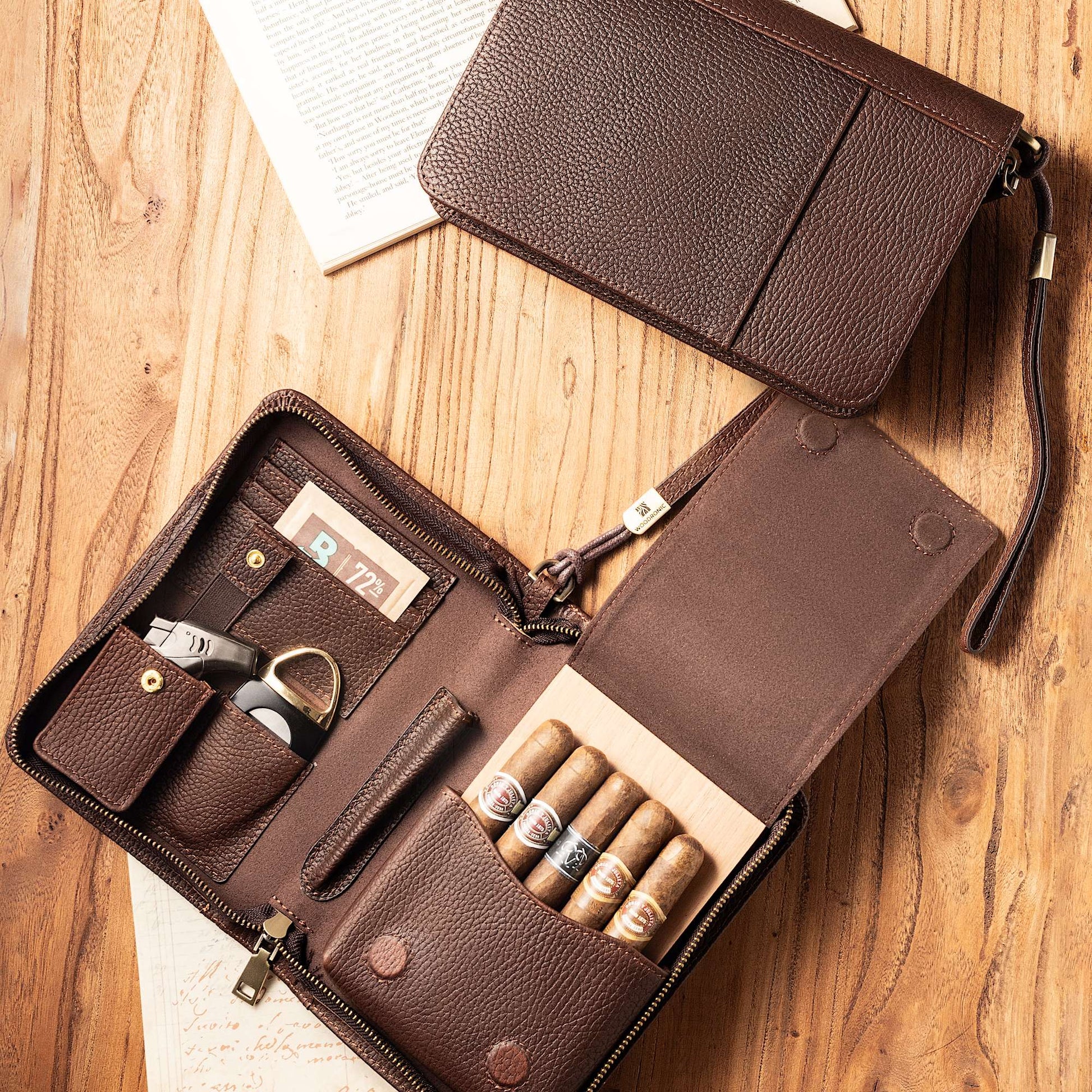 Open leather cigar case laid on a rustic wooden table, displaying its organized interior with five premium cigars, cutter, lighter, and humidifier, styled with vintage book pages.